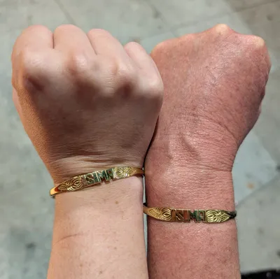 Two hands with matching bracelets that say isima
